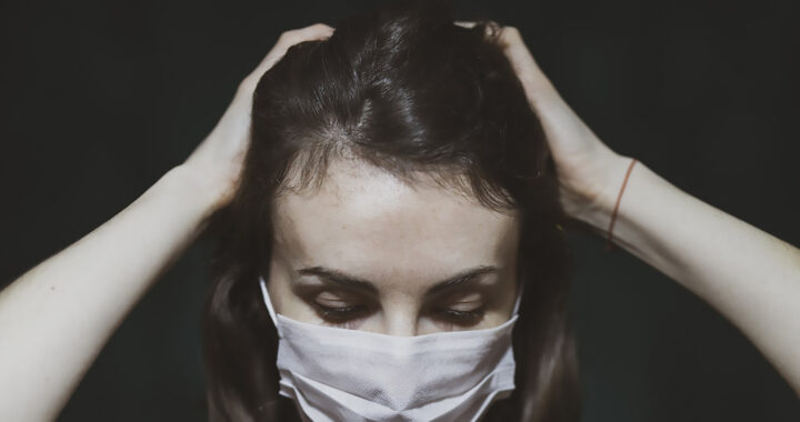 A seemingly distressed woman wearing a facial mask for the article "Long COVID is Affecting the Financial Health of Americans"